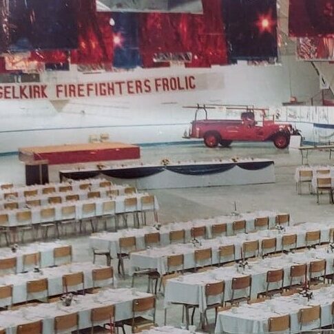 Firefighters Frolic at the Selkirk Centennial, 1982, Ted Wozny Colour image of several tables and chairs set up in the Selkirk Arena. The ceiling and background is decorated with red and blue streamers