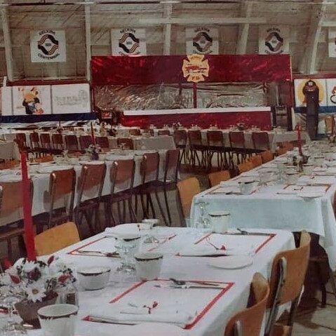 Firefighters Frolick Tables Centennial, 1982, Ted Wozny Colour image of tables and chairs at the Firefighter's Frolic at the Selkirk Arena. Selkirk Centennial logos can be see in the background. Flowers are on the tables