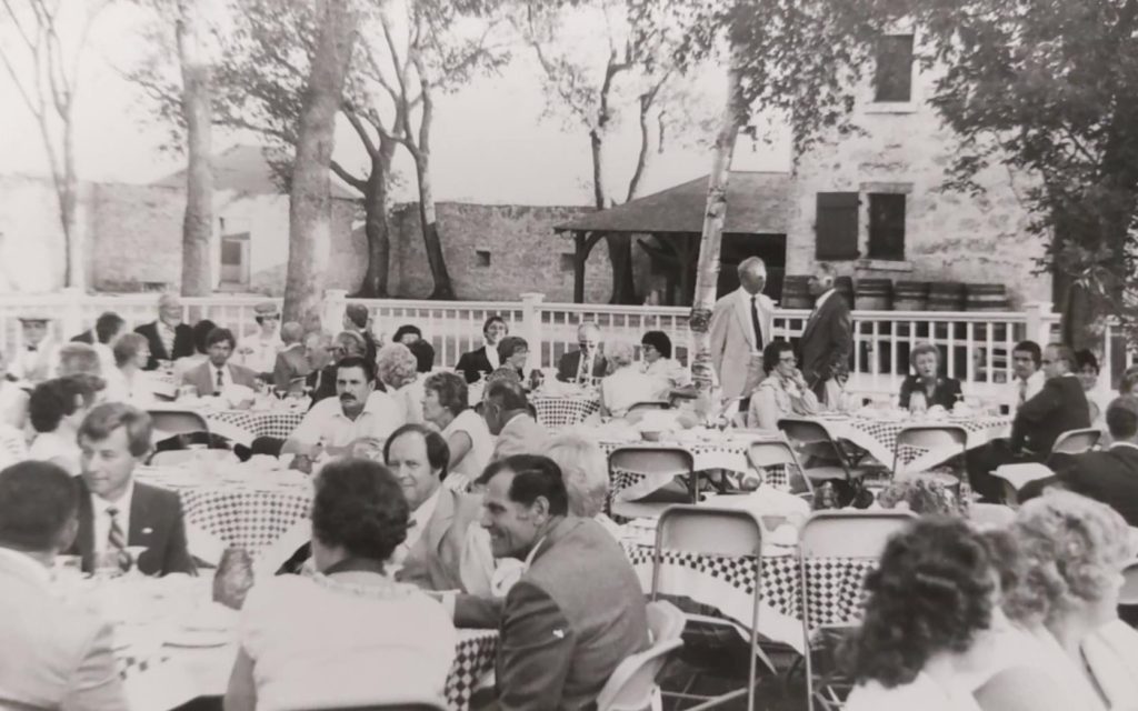 Black and white image of the Governors Dinner at Lower Fort Garry. Image shows people dressed in formal attire and seated at tables in the yard