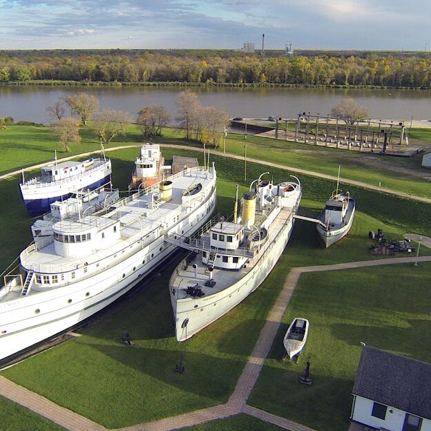 Jackie S Far Right Corner, c2017, Marine Museum of Manitoba Aerial photo of the Marine Museum which shows four white boats in differing sizes and walkways between them on the green grass. The boats are docked