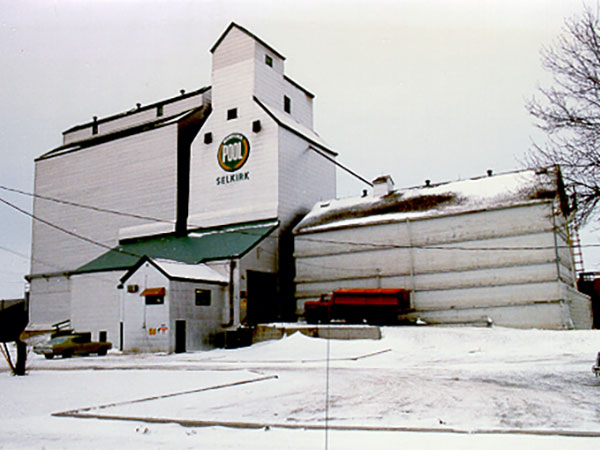 Colour photo of a grain elevator in the winter. There is snow on the ground