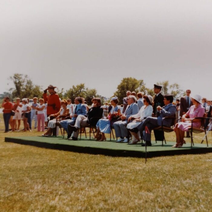 Princess Anne at Selkirk Park, 1982, Selkirk Museum Colour image of a green stage set on the grass. A RCMP officer if on the right hand side. Princess Anne sits on the platform at the center of the stage