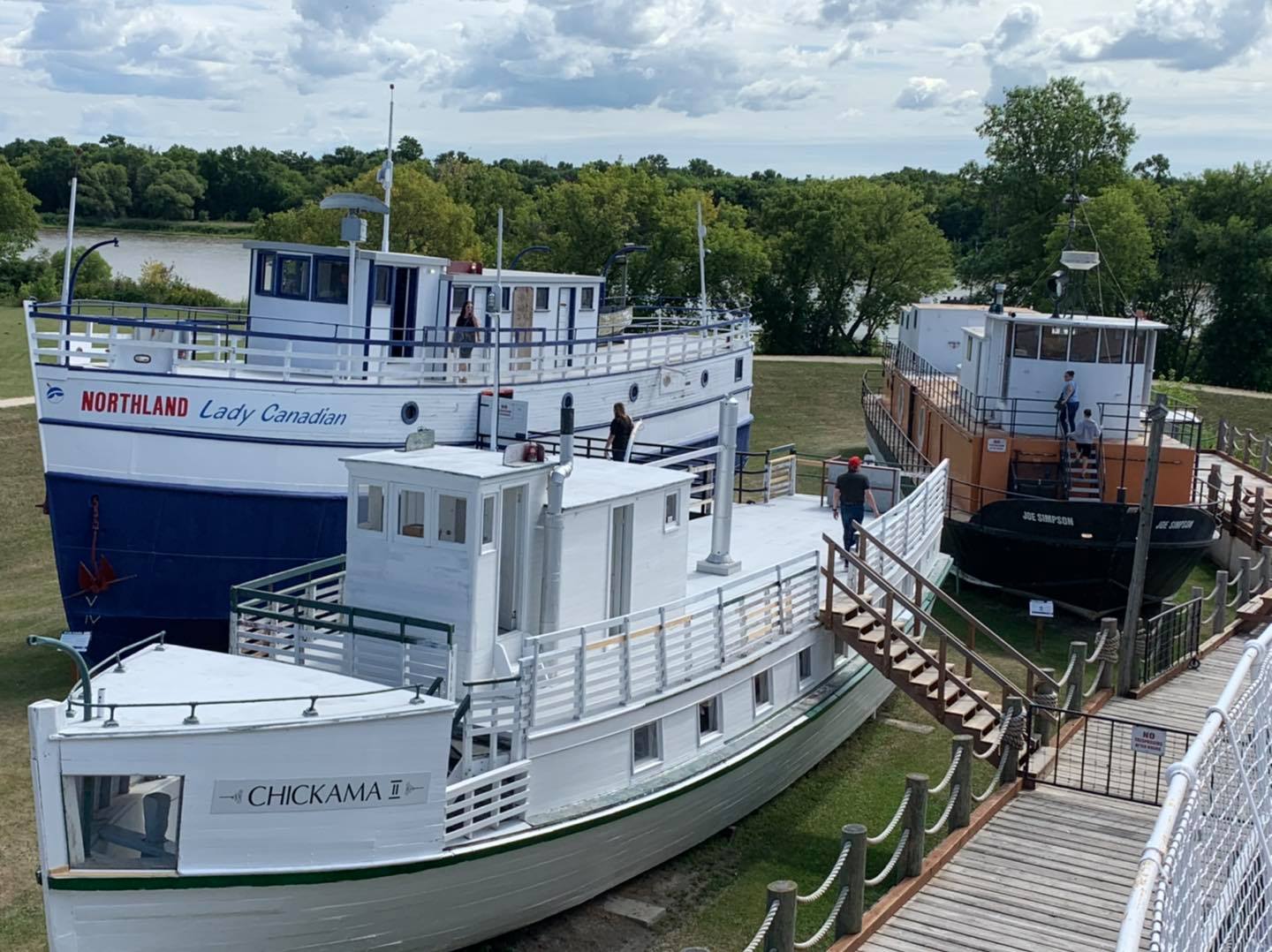A colour image of two small white boats. Both are docked on the grass and one has a staircase leading to a wooden boardwalk