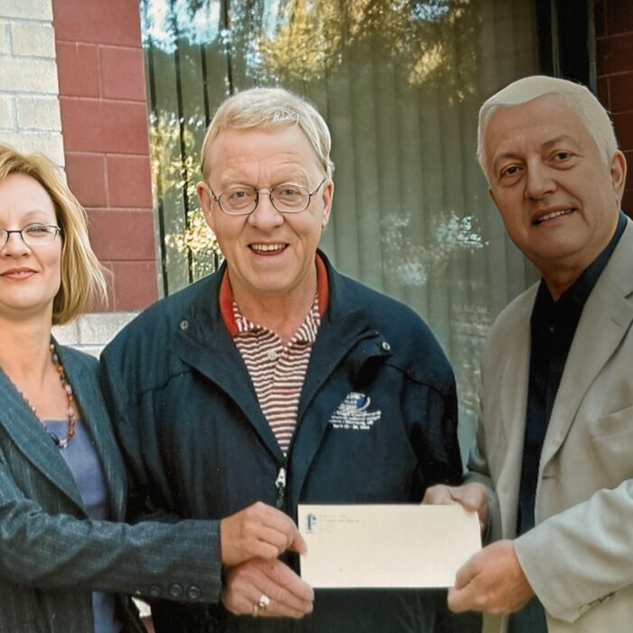 Bev Clegg and Frank Wellink Accept a $20,000 Cheque from Bob Jefferson to Fund a New Scholarship, 2009, Selkirk District Community Foundation A woman with short blond hair stands next to a man with grey hair and glasses. On the far right is another man with white hair. They all hold a cheque.
