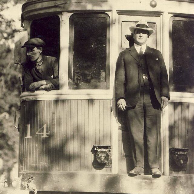 Black and white image of a man standing on the end of a train