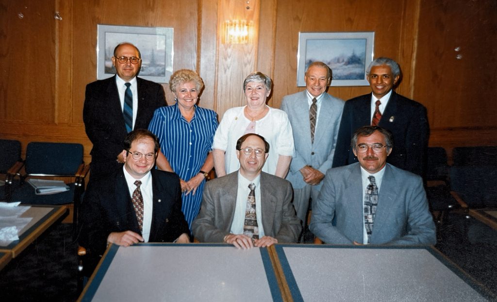 A group of people sitting and standing behind a table. The people are the first board of directors