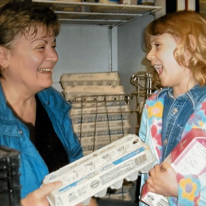 Food Bank Chair Pat Bird and Amelie, 2009, Selkirk District Community Foundation A woman holds a carton of eggs and smiles at a young girl holding a carton of milk