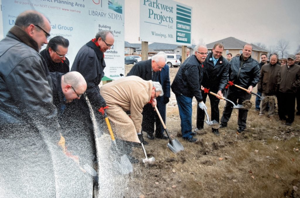 A group of men stand around grass and push shovels into the ground