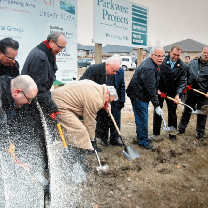 A group of men stand around grass and push shovels into the ground