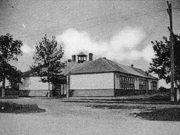 A black and white photo of South Ward school from an angle. There are trees on either side of the school