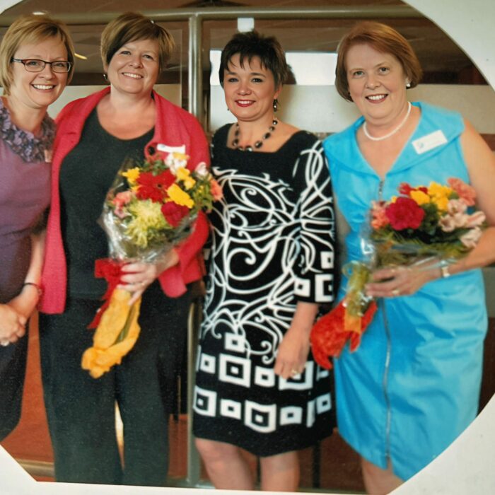 Thank You to Bev Clegg, Lesli Malegus, Kelly Lewis, Bev Stewart, Date Unknown, Bev Clegg A group of four women stand together. Two of the women hold bouquets of yellow and red flowers.