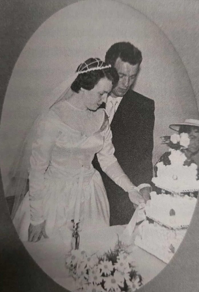 Black and white image of a bride and a groom cutting their wedding cake. The wedding cake is three tiers and white frosting