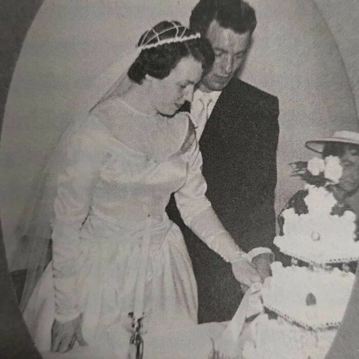 Just Married, 1956, According to Me by Dawn Anderson MacFarlane Black and white image of a bride and a groom cutting their wedding cake. The wedding cake is three tiers and white frosting