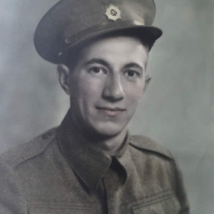 Colour image of a young man, Allan Sinclair, seated smiling at the camera. He is wearing a military jacket with a hat