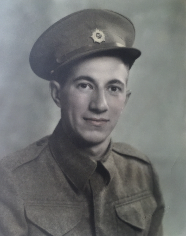 Colour image of a young man, Allan Sinclair, seated smiling at the camera. He is wearing a military jacket with a hat