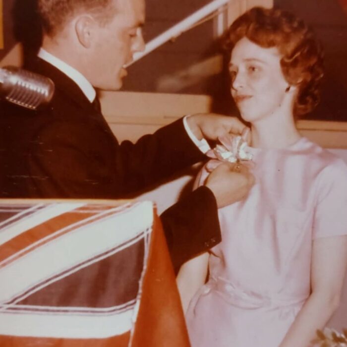 Colour image of a man pinning a corsage to a woman's dress. There is a podium in the foreground with a British flag hunt on it