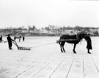 A black and white image of men and horses on the river. The river ice is cut into a grid
