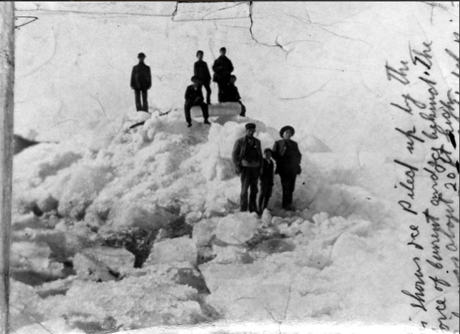 A black and white image of seven men and boys standing on a large pile of snow