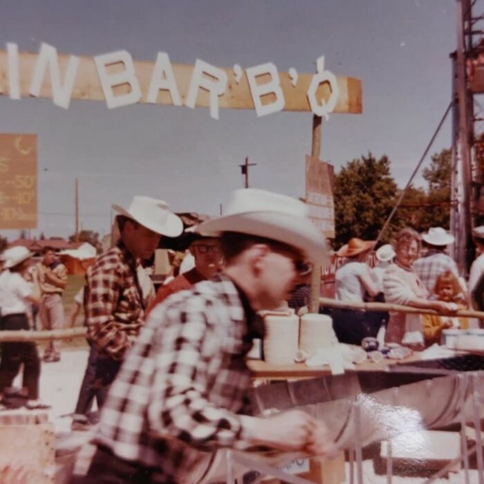 Colour image of a group young man working at a table. In the background is a sign which reads 'KIN BAR'B'Q'