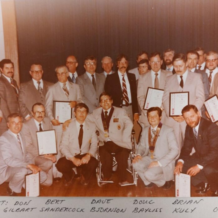 A colour image of a group of men sitting and standing in a large group. Some of them are holding certificates
