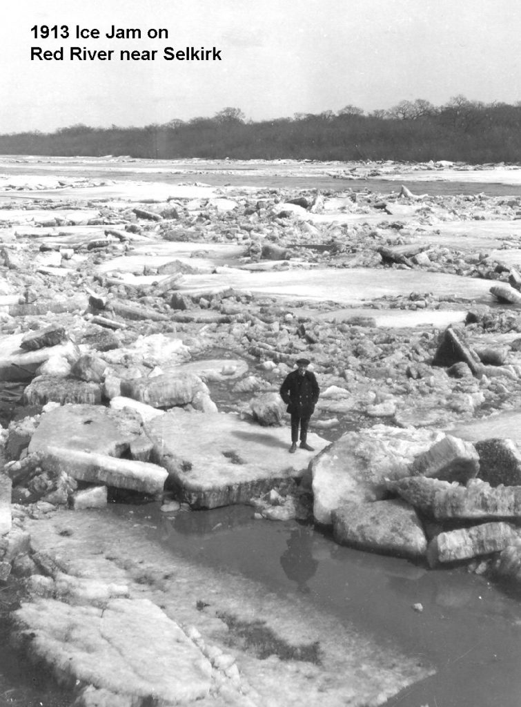 A black and white image of a man standing on the river. There are large chunks of ice broken up floating on the water