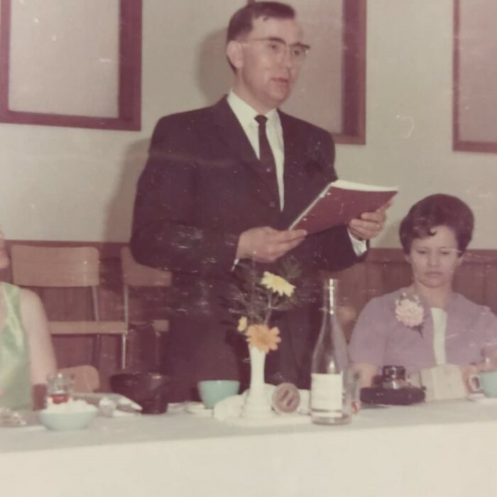 Colour image of a man standing at a table holding a book