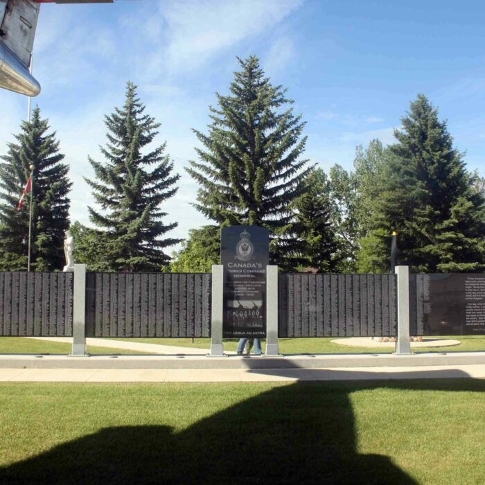Bomber Command Memorial Wall with PO Charles Anthony Griffiths, Nanton AB, Date Unknown, American War Memorials Overseas Inc. Colour photo of a memorial wall with names listed on each panel. There are large evergreen trees in the background