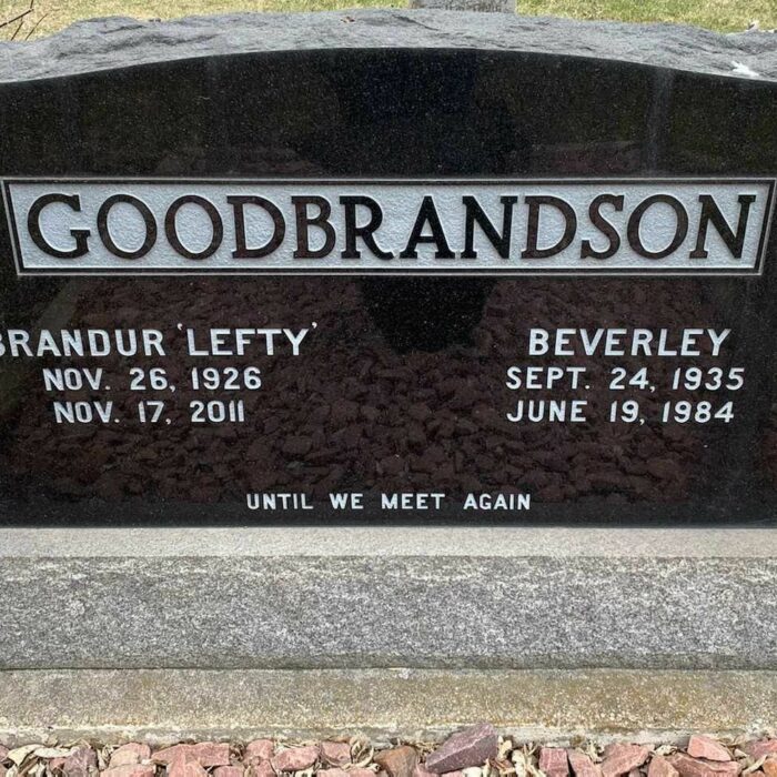 A colour image of a gravestone. The stone is black with white lettering. The family name 'Goodbrandson' is in capital letters across the top of the stone. Beneath the family name is both 'Brandur 'Lefty'' and 'Beverly' along with their birth and death dates.