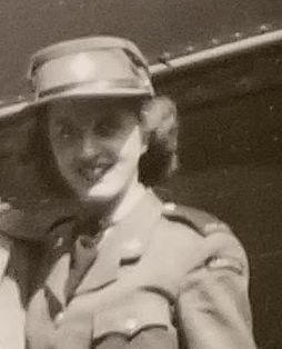 Black and white image of a woman in military uniform. She has short curly hair and wears a hat. She is looking at the camera and smiling