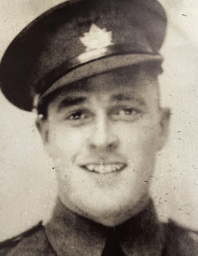 Black and white image of a man in military uniform. The photo is taken from the shoulders up. The man wears a hat and smiles at the camera
