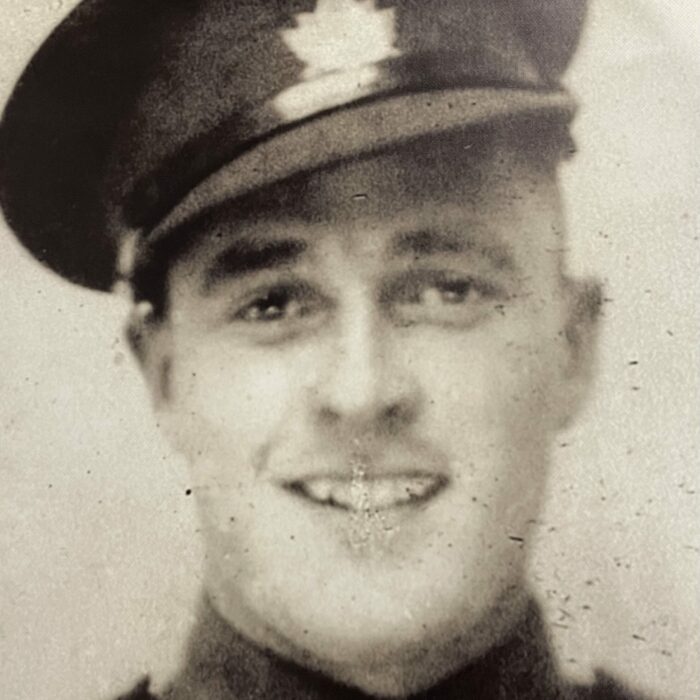 Black and white image of a man in military uniform. The photo is taken from the shoulders up. The man wears a hat and smiles at the camera