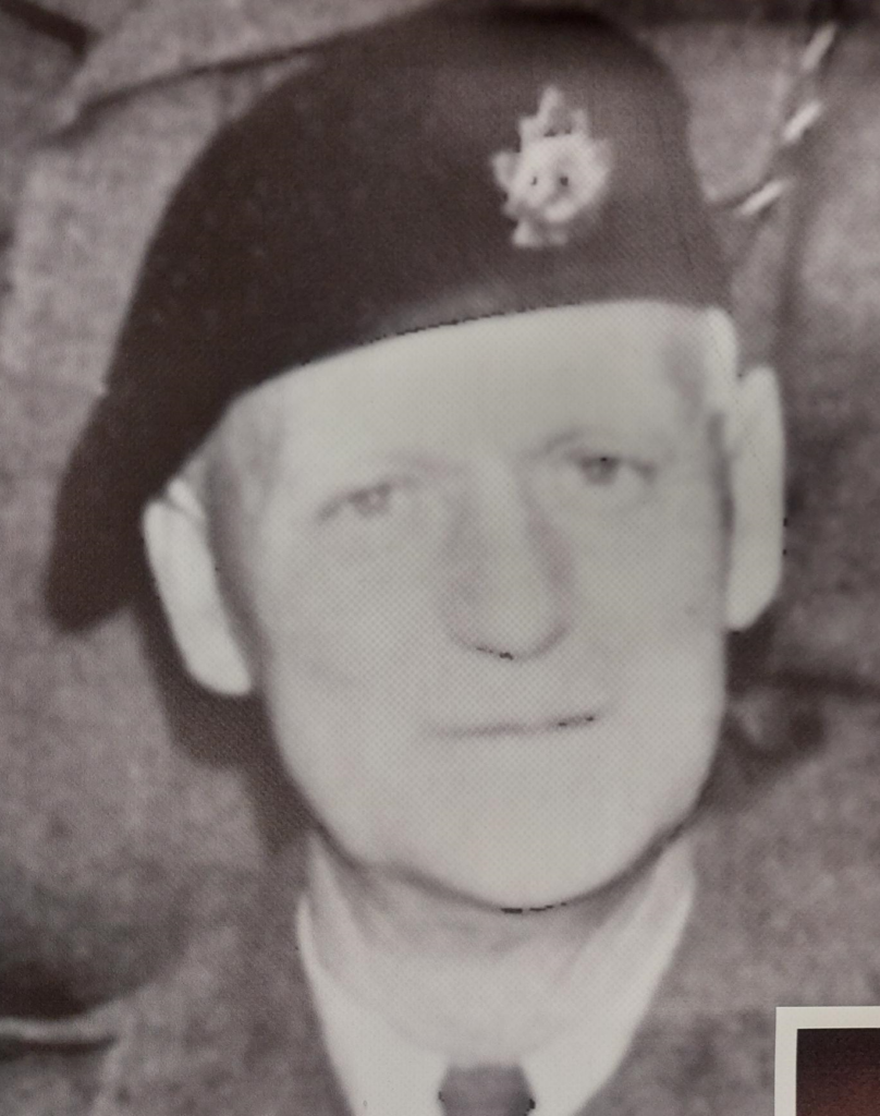 A black and white image of a man in military uniform. The photo is taken from the shoulders up. The man looks at the camera