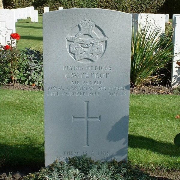 Colour image of a gravestone. In the background is grass, plants, and white crosses