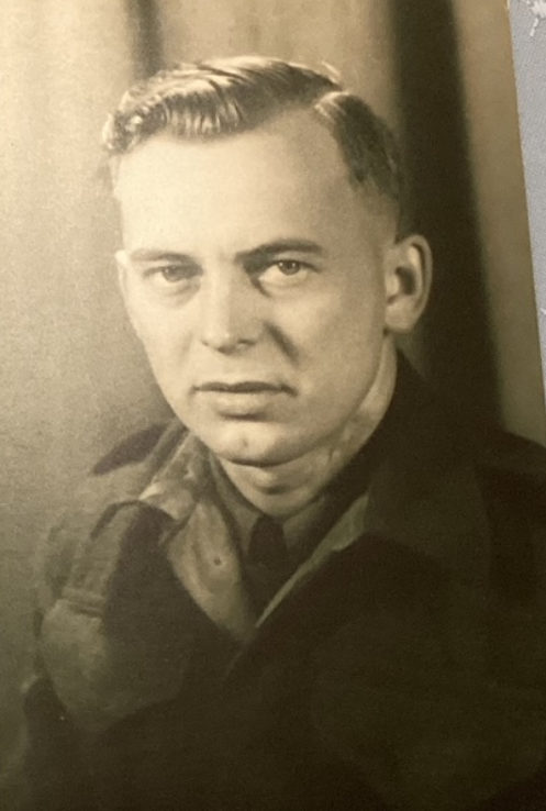 A black and white image of a man wearing a military jacket. He looks at the camera unsmiling. The photo is taken from the chest up