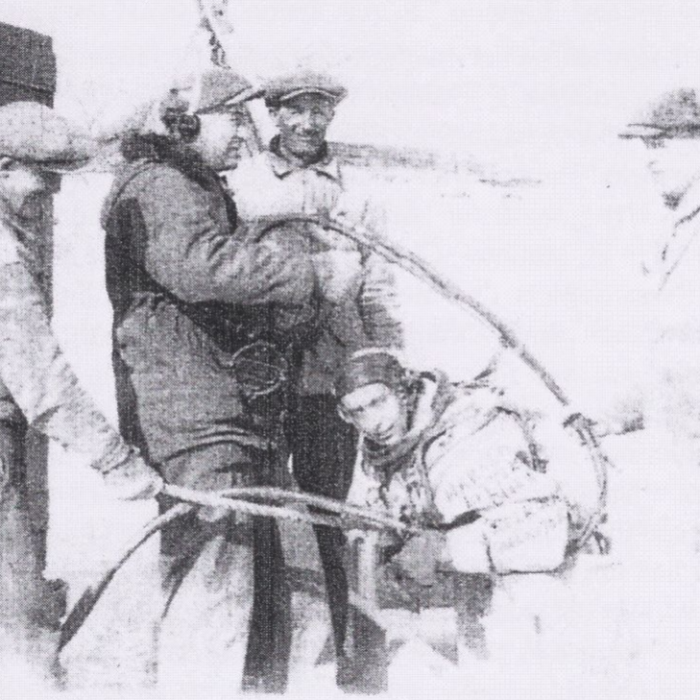 Black and white image of three men helping a scuba diver down into the river