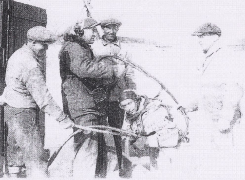 Black and white image of three men helping a scuba diver down into the river