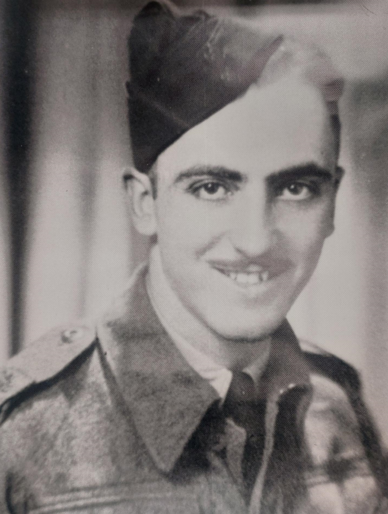 Black and white photograph of Jim Laye. He is dressed in military uniform and looks at the camera. He has a moustache and smiles.