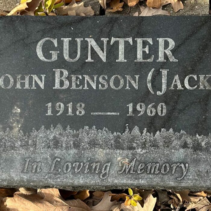 A colour image of a gravestone. The stone is dark grey with white lettering.
