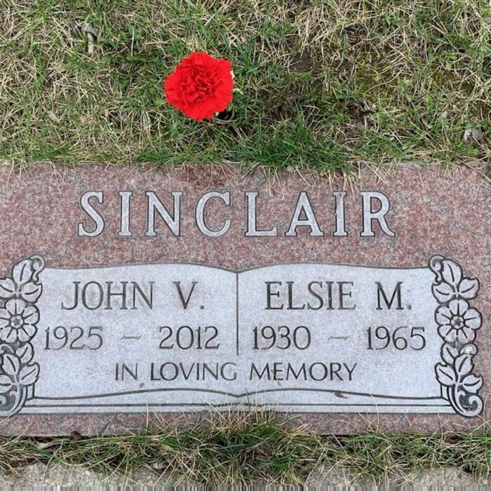 John V. Sinclair Gravestone, 2022, Find A grave Colour image of a gravestone which reads 'Sinclair' at the top. Then the names 'John V. and 'Elsie M.' along with their birth and death dates. The stone is red withe a red flower in the grass above the stone