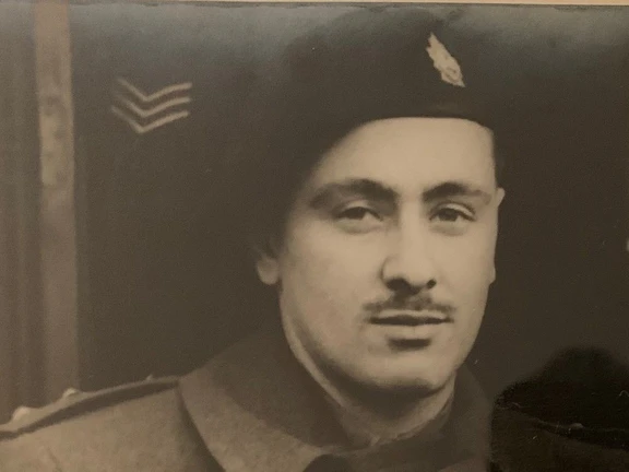 A black and white photograph of a soldier in uniform. He wears a hat, jacket, has a moustache and looks directly at the camera