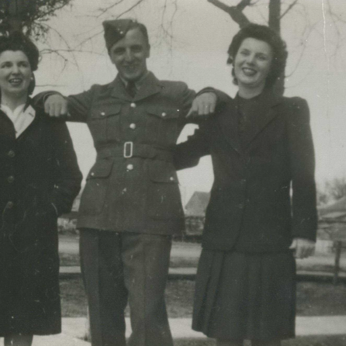 Mary, Jack, Leana, c1942-1945, Acnestry.ca A black and white image of a woman, John (Jack) Cy Laye, and another woman. The man stands at the centre of the two women with his arms on their shoulders. He is in military uniform. The women both wear dark skirt suits with jackets. The woman on the right has her arm around the mans back. All three smile at the camera