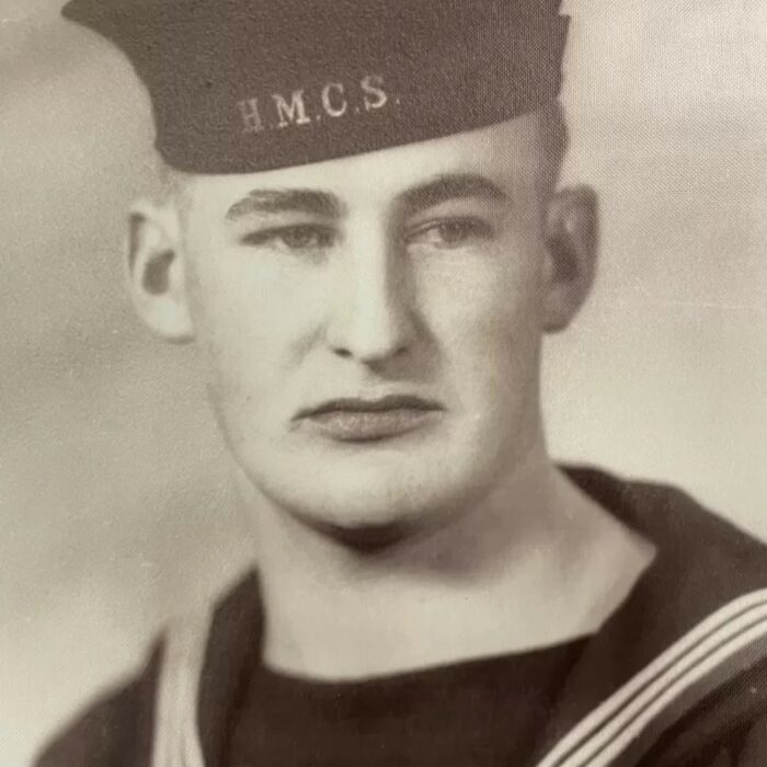 A black and white image of a young man in navy uniform. He looks to the right of the camera