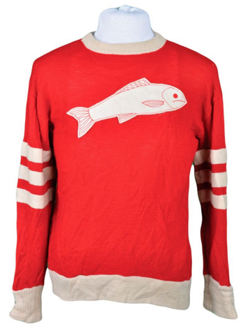 A colour image of a red hockey jersey. On the jersey is a white fish and three white stripes on both sleeves