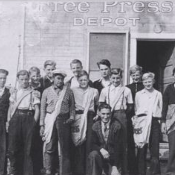 Black and white image of a group of young men and boys standing outside of a building.