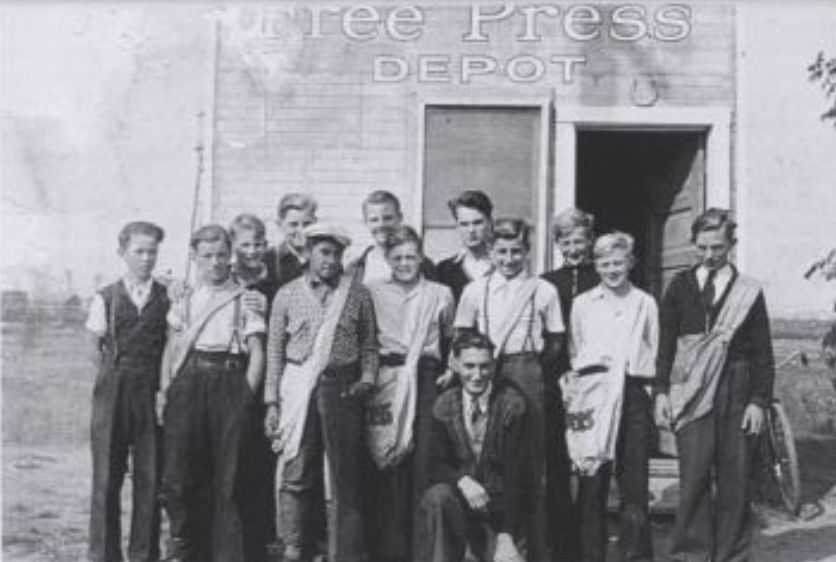Black and white image of a group of young men and boys standing outside of a building.