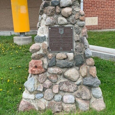 Cairn infront of École Selkirk Junior High School, 2024, Selkirk Museum Collection A colour image of a stacked stone 'cairn' with a metal plaque on the face of the cairn.