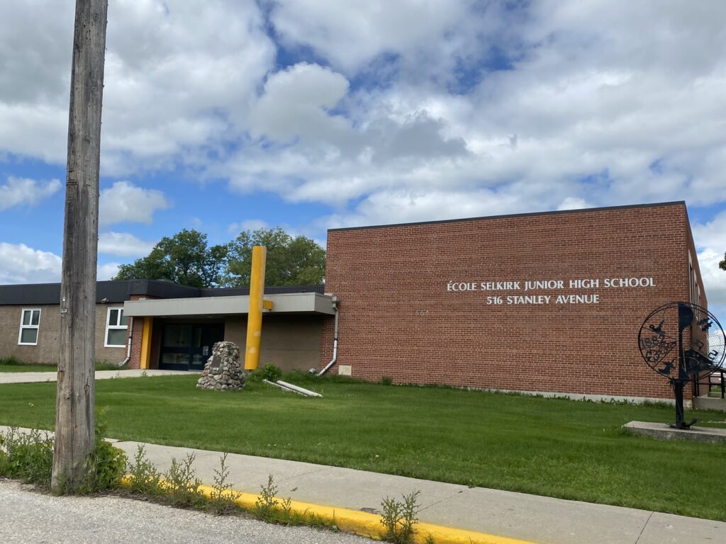 Colour image of a school. On the right side of the image is a large brick gymnasium. On the left is the school's entrance
