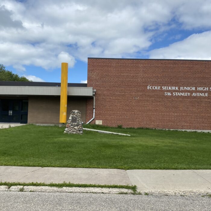 École Selkirk Junior High and Cairn, 2024, Selkirk Museum Collection Colour image of a school. On the right side of the image is a large brick gymnasium. On the left is the school's entrance
