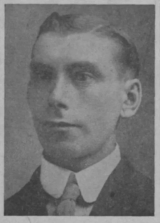 Black and white photo of a middle-aged man who is wearing a suit and tie. He looks to the left of the camera