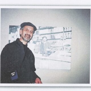 Colour photo of a man standing next to a photo of a young child. The man wears a jacket and a hat. He has a beard